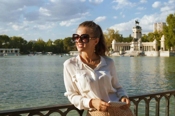 smiling elegant woman in white blouse and shorts at Retiro Park in Madrid, Spain using smartphone for information sharing and networking or getting virtual travel agent help. adventure travel.