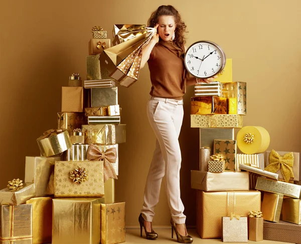 穿着金色米色裤子和棕色衬衫 在2堆金色礼物中的购物袋和时钟 穿着时髦的时尚怪物 缺乏时间的概念 为大家寻找节日礼物 — 图库照片