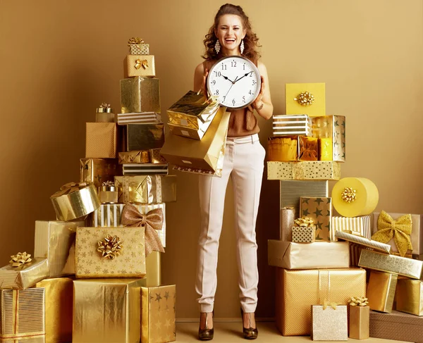 ゴールド ベージュのズボン 茶色のブラウスの若いファッション屋を浮かべてショッピング バッグ プレーンの壁の前に黄金の贈り物 杭の中で時計を表示の完全な長さの肖像画 最初分ショッピング — ストック写真
