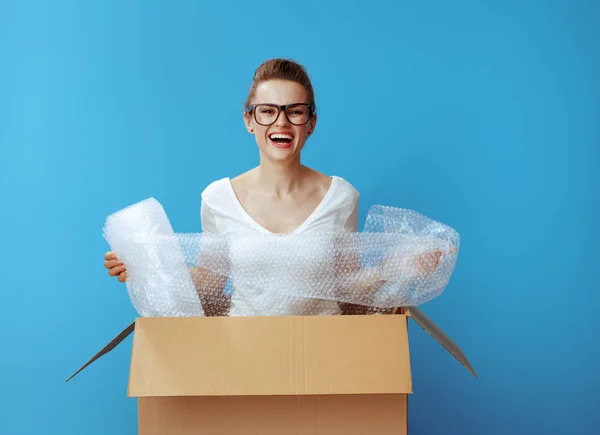 青い背景に対して空気泡フィルム包装材と段ボール箱に白い シャツで幸せな現代の女性 — ストック写真