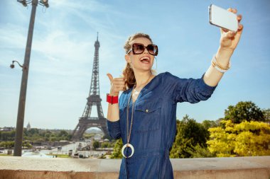Mavi Jeans başparmak gösterilmesini ve smartphone ile selfie Paris, Fransa'da alarak genel mutlu son moda kadın.