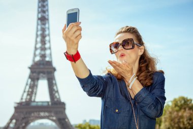 Mavi Jeans genel telefon ile selfie alarak ve hava üfleme Trocadero Paris, Fransa'da Eyfel Kulesi manzaralı, öp mutlu modern kadın.
