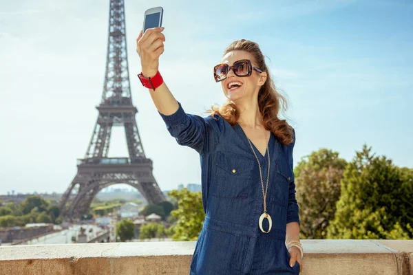 微笑时尚的旅行者妇女在蓝色牛仔裤整体采取自拍手机在巴黎 — 图库照片