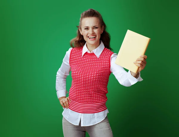 Sorrindo estudante ajuste mostrando livro amarelo no fundo verde — Fotografia de Stock