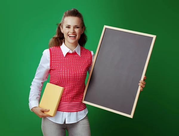 Happy fit student with yellow book showing black chalkboard — Stock Photo, Image