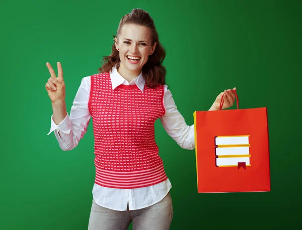 Estudiante feliz con bolsa de compras roja con libros que muestran la victoria —  Fotos de Stock