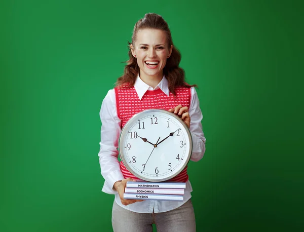 Smiling learner woman showing textbooks and white round clock — Stock Photo, Image