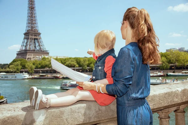 流行の母親とマップを保持していると指摘 フランスのエッフェル塔を望むセーヌ川の堤防で欄干近く観光客を娘の後ろから見てください — ストック写真