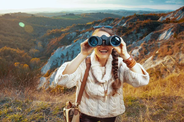 smiling active woman hiker looking in camera through binoculars