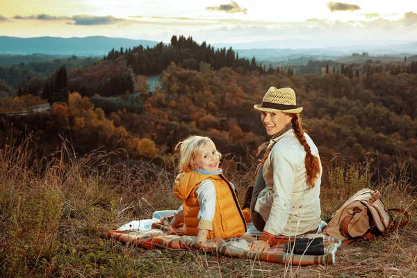 Mãe feliz e criança na Toscana ao pôr do sol sentado em cobertor — Fotografia de Stock