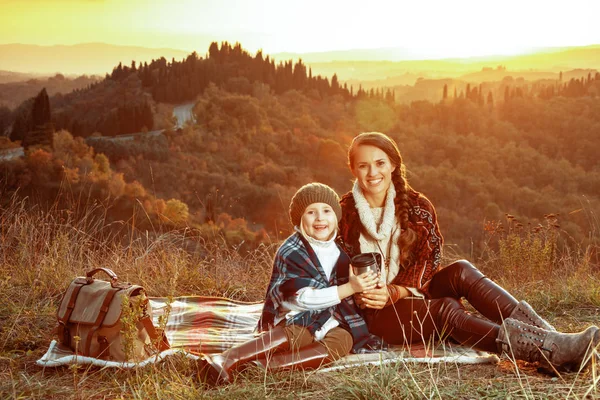 Usmívající se matka a dítě sedí na dece s Termoska Hrnek — Stock fotografie