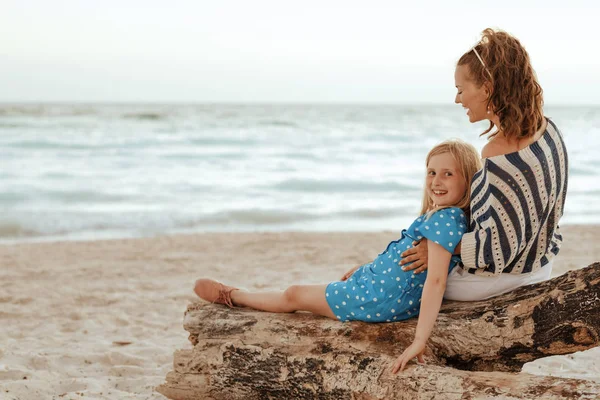 Matka a dítě sedí na dřevěných zádrhel na pláži večer — Stock fotografie