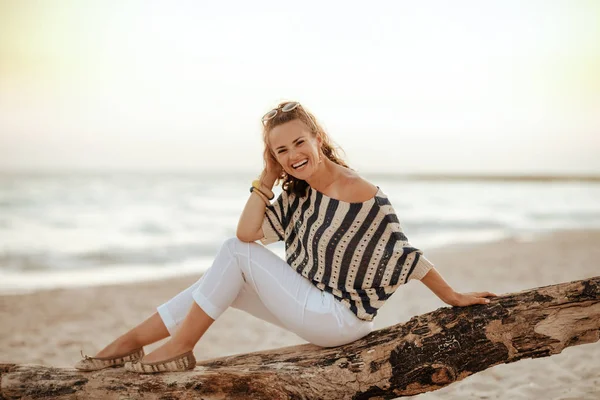 Reiziger vrouw zitten op houten addertje onder het gras aan kust in avond — Stockfoto