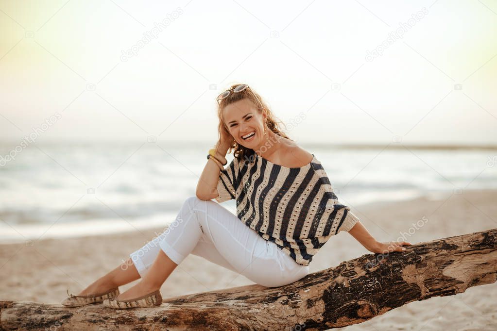 traveller woman sitting on wooden snag on seashore in evening