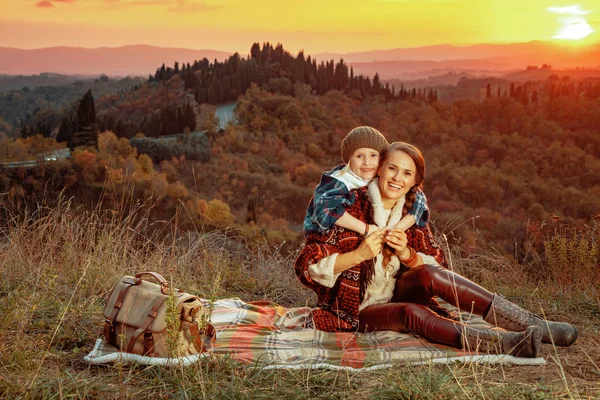 Smilende mor og datter krammer mens du sidder på tæppe - Stock-foto