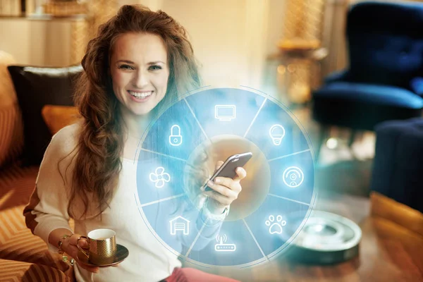 Mujer con taza de café utilizando la aplicación para el hogar inteligente en el teléfono inteligente — Foto de Stock