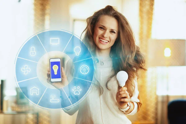 Mujer mostrando aplicación casera inteligente en el teléfono inteligente y la lámpara inteligente — Foto de Stock