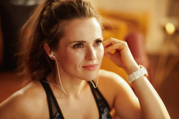 放松活跃的运动女子穿着健身服 在现代客厅用耳机听音乐 — 图库照片