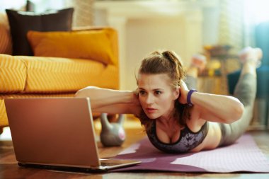 modern evde spor giysiler sağlıklı spor kadın sosyal medya egzersiz sonuçlarını paylaşmak için dizüstü bilgisayar kullanarak ve fitness mat abs egzersizleri yapıyor.