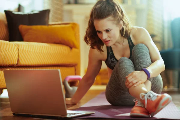 在现代客厅里穿着运动服的年轻女运动员用笔记本电脑在社交媒体上分享锻炼结果 — 图库照片