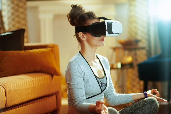 Closeup on active sports woman in sport clothes in the modern house doing yoga in VR gear.