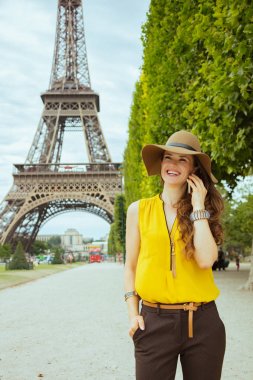 Paris'te Eyfel kulesine bakan Champ de Mars sarı bluz ve şapka gülümseyen genç gezgin kadın, Fransa bir cep telefonu ile konuşan.