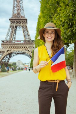 Paris'te Eyfel kulesine bakan Champ de Mars'ta sarı bluz ve şapka ile mutlu modern gezgin kadın, Fransa.