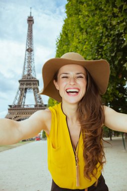 sarı bluz ve şapka ile gülümseyen genç turist kadın Paris'te Eyfel Kulesi net görünümüne karşı selfie alarak, Fransa.