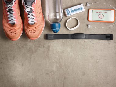 Spor ayakkabılar, kalp atış hızı monitörü, su şişesi, beyaz fitness izci, kulaklık, ham protein çubuğu, kalp atış hızı uygulaması zemin döşeme akıllı telefon üzerinde closeup.