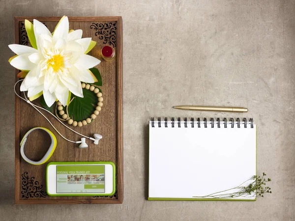 Closeup on tray with fragrant stuff for aroma yoga, beads, fitness tracker, headphones and smartphone with personal yoga trainer app and opened notebook with pen laying on the floor.