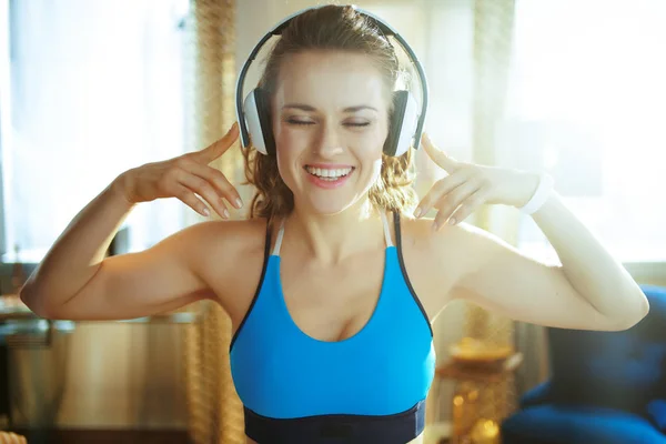 Mosolygós nő, aki a modern otthoni fejhallgatóval zenét hallgat — Stock Fotó