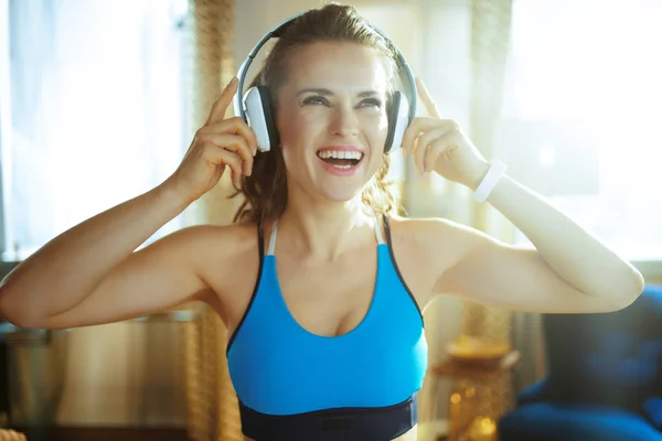 Mujer deportiva escuchando música con auriculares en casa moderna —  Fotos de Stock