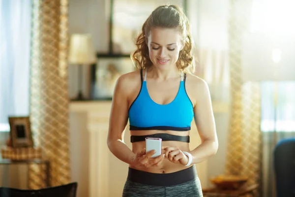 Woman wearing heart rate monitor using fitness app in phone — 스톡 사진