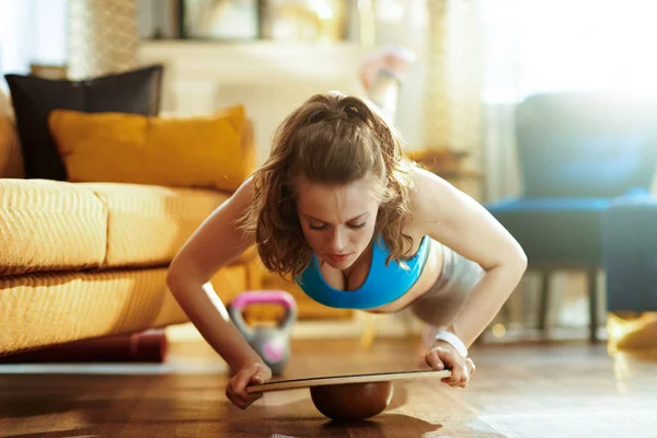 Mujer en la sala de estar moderna haciendo flexiones utilizando el tablero de equilibrio —  Fotos de Stock