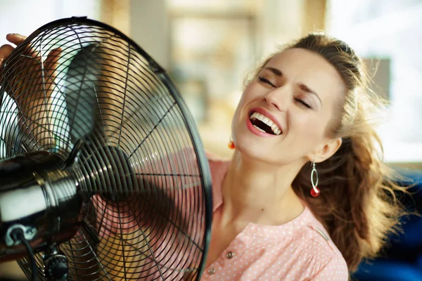 Усміхнена стильна жінка використовує металевий вентилятор для підлоги — стокове фото