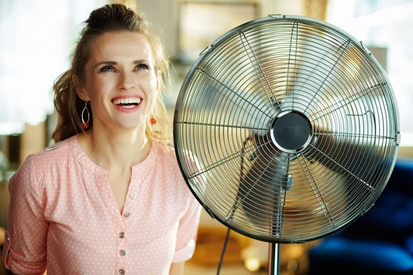 Усміхнена елегантна домогосподарка біля металевої підлоги стоячого вентилятора — стокове фото