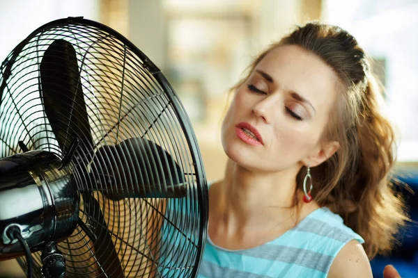 Descontraído moderna dona de casa desfrutando de frescura na frente do ventilador — Fotografia de Stock