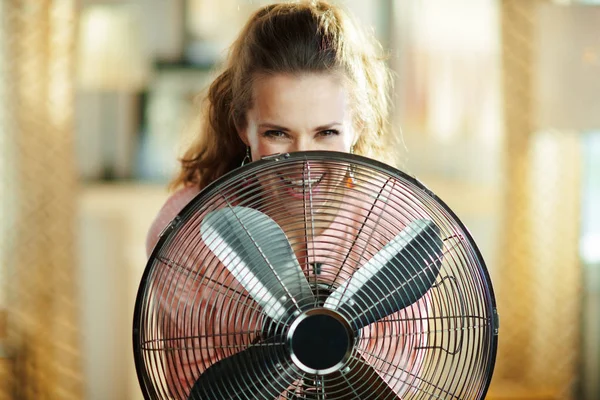 Sorrindo jovem mulher olhando para fora do ventilador metálico elétrico — Fotografia de Stock