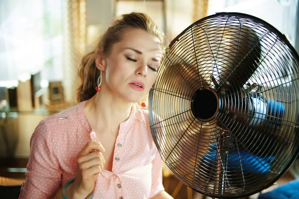 Женщина наслаждается ветром рядом с вентилятором, страдающим от летней жары — стоковое фото