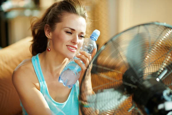 Hete vrouw met een fles koud water met behulp van elektrische metalen ventilator — Stockfoto