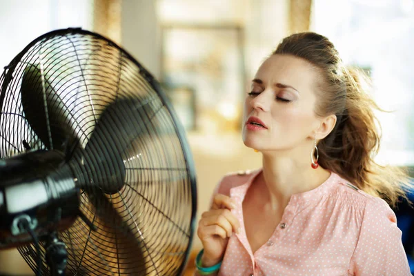 Joven ama de casa disfrutando de frescura en frente de ventilador de trabajo — Foto de Stock