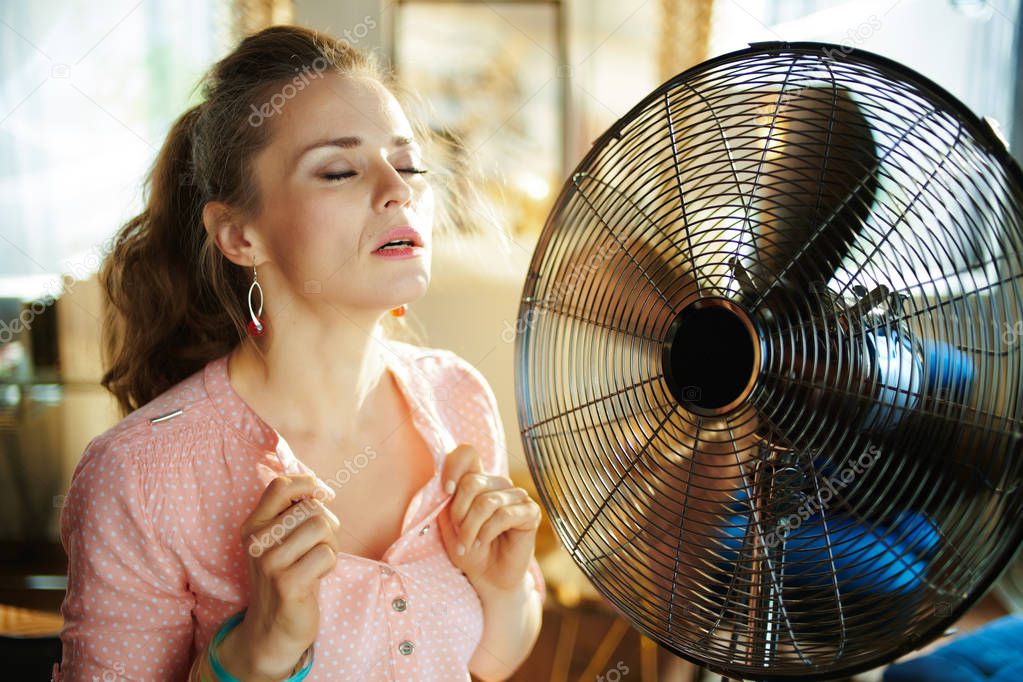 woman enjoying freshness near fan suffering from summer heat