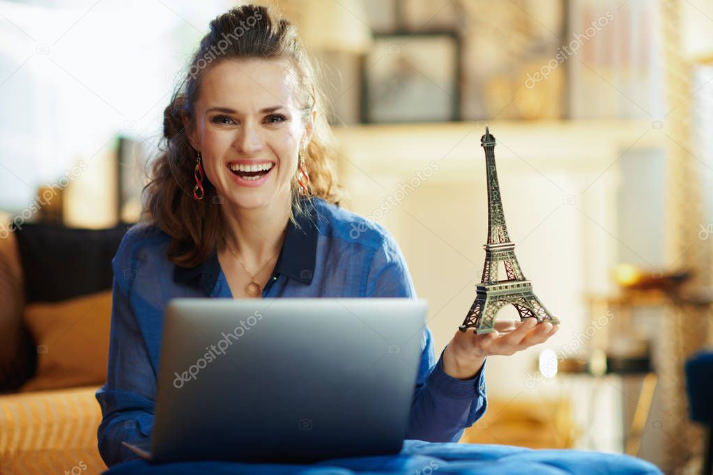 smiling stylish woman with souvenir of eiffel tower with laptop