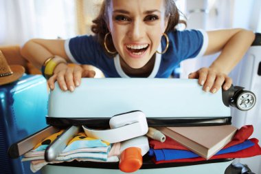 paketlenmiş bavul üzerinde kapatmaya çalışan gülümseyen şık kadın