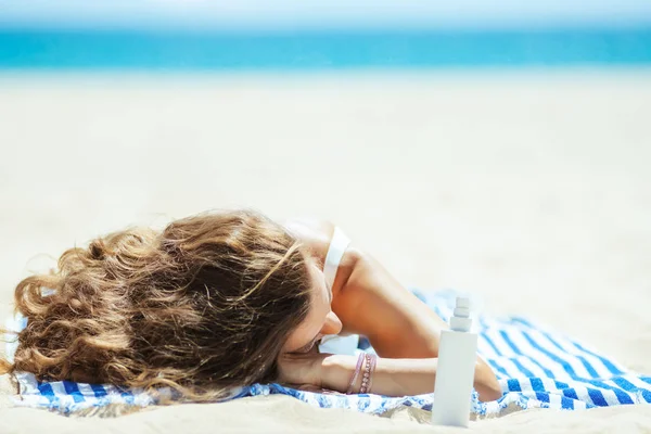 ストライプタオルに寝そべてる日焼けローションを持つ健康な女性 — ストック写真