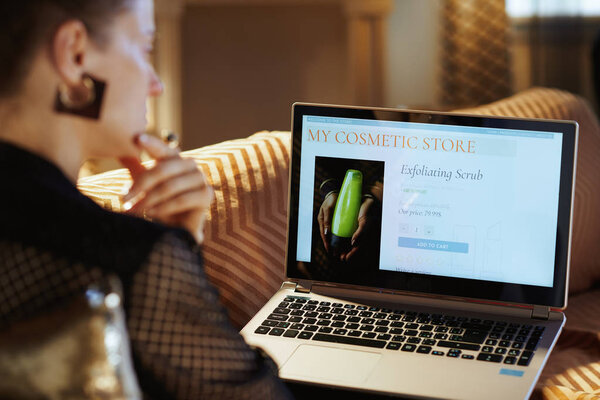 pensive housewife using beauty cosmetics online store on laptop