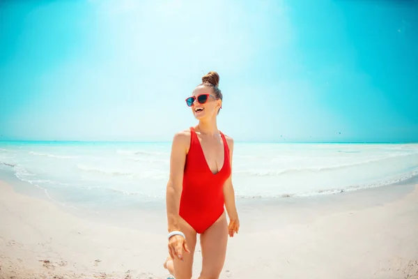 해변 산책에 빨간 수영복을 입고 웃고있는 젊은 여성 — 스톡 사진