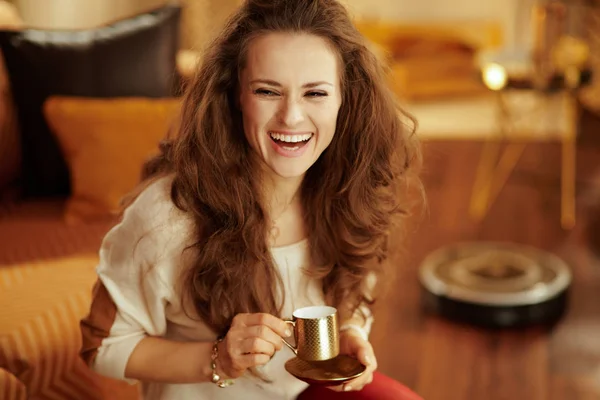 Sorrindo mulher bebendo café enquanto robô vácuo limpeza chão — Fotografia de Stock