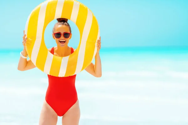 Woman on seashore looking through yellow inflatable lifebuoy — Stock Photo, Image