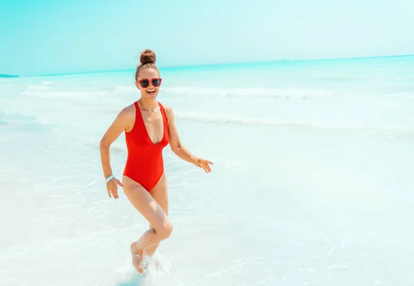Felice giovane donna in costume da bagno rosso sulla spiaggia in esecuzione — Foto Stock